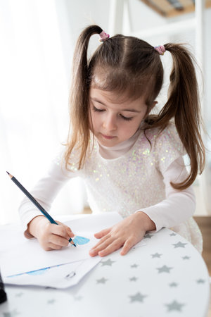 Cute little girl enjoys painting. Girl drawing and coloring picture with color pencil in her room at...