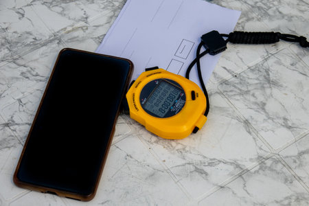 Professional sports timing setup with a yellow digital stopwatch, smartphone, and scorecard. Concept of competition, training, speed, and precision for a coach or athlete.の写真素材