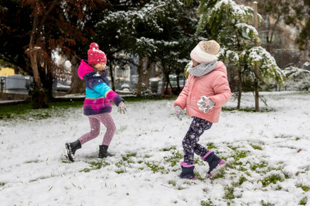 Two little girls playing games and having fun, having a snow ball fight in the snow. Happy children play snowballsの写真素材