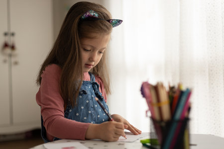 Cute little girl enjoys painting. Girl drawing and coloring picture with color pencil in her room at homeの写真素材