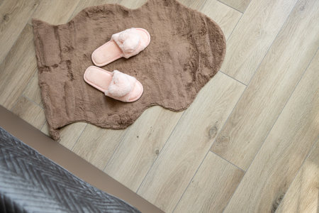 Cozy Pink Fluffy Slippers on Soft Brown Rug and Wooden Floor. Warm Comfortable Footwear for Relaxation, Home Interior Lifestyle, Bedroom Comfort Conceptの写真素材