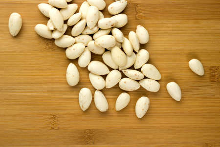 Closeup of raw blanched almonds scattered against a wooden cutting boardの写真素材