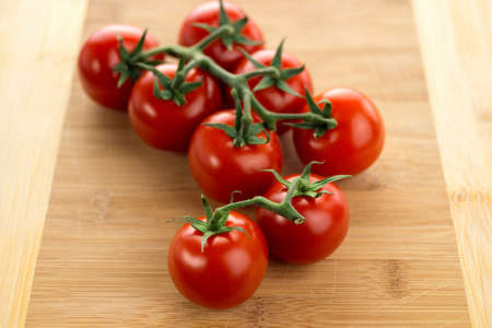 Red ripe cherry tomatoes with vines on a wooden cutting board. Macro view with shallow depth of field.の写真素材