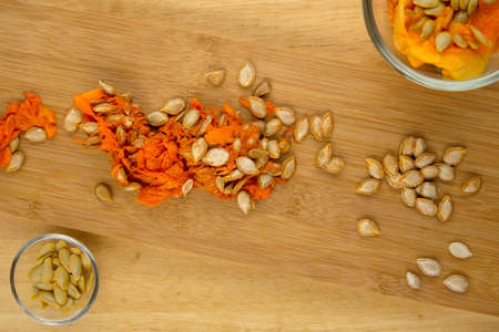 Bowls of pumpkin seeds and flesh on wooden boardの写真素材