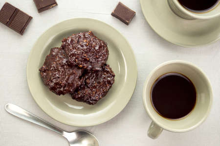 Rich chocolate cookies in a saucer next to cups of black coffee and chocolate piecesの写真素材
