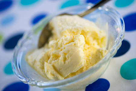 Closeup of ice cream in a clear bowl with spoon against a spotted birthday or party background.の写真素材
