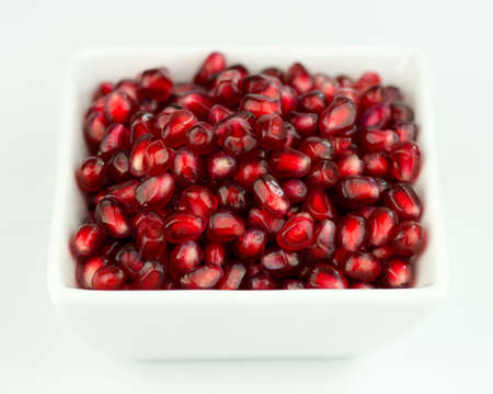 Macro of red pomegranate seeds in white bowl on whiteの写真素材