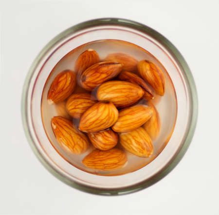 Closeup of raw almonds soaking in a glass bowl of water, isolated on a white backgroundの写真素材