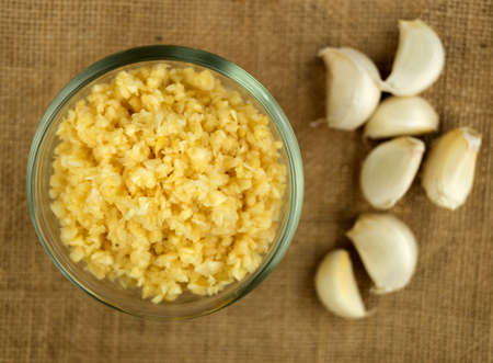 Aerial macro of finely chopped garlic in a bowl against gunny cloth with whole garlic cloves in the backgroundの写真素材