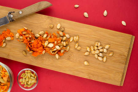 Wooden cutting board with orange squash seeds against red backgroundの写真素材