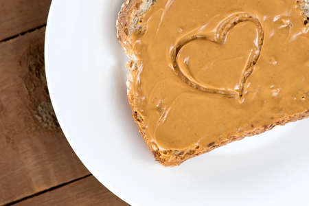 Peanut butter toast with heart shape on white against wooden boardの写真素材