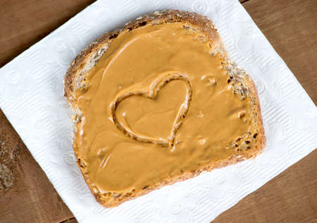 Tosted peanut butter sandwich on tissue against wooden board with heart shape