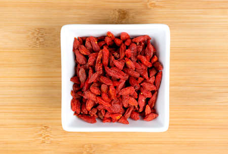Macro of dehydrated red goji berries in white bowl against wooden boardの写真素材