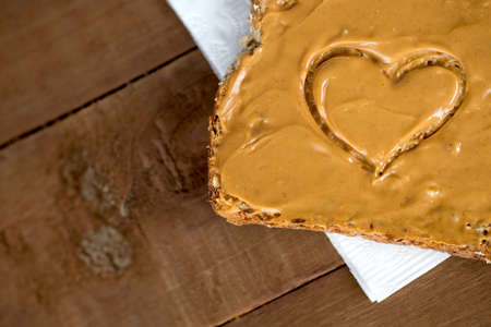 Closeup of peanut butter toast with heart shape on tissue against woodの写真素材