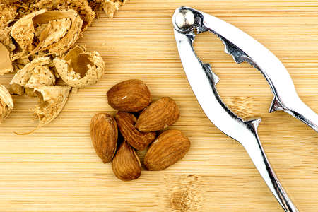 Almonds, shells with metal nut cracker on wooden backgroundの写真素材