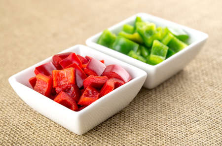 Chopped up red bell pepper in foreground and green capsicum in backgroundの写真素材