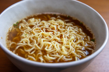 Instant noodles in a bowl on a wooden table, top view.