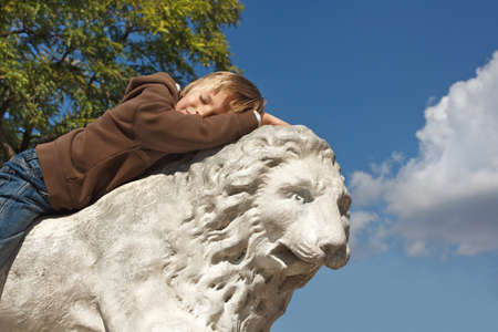Boy resting on a stone lion outdoorの写真素材