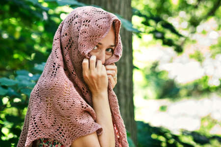 Smiling girl hides her face under a knitted shawl