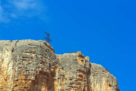High rock against the blue cloudless sky. On the cliff is no vegetation. At the top is a column power lineの写真素材