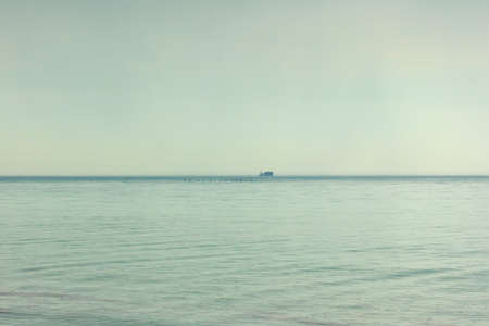 At sea, the rain. ozhdlivaya gray weather. Seascape. On the horizon is a cargo ship, a cargo ship. Foggy weather. Over the edge of the sea flying flock of birds. Flock of ducks.の写真素材