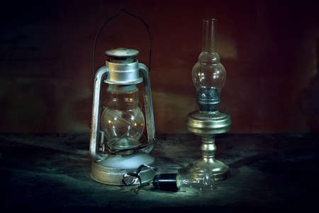 Vintage lights lie on the old wooden table. Broken light bulb with holder and wire. Kerosene lamp, kerosene lantern bat. The photo was taken using a light brush effect it.の写真素材