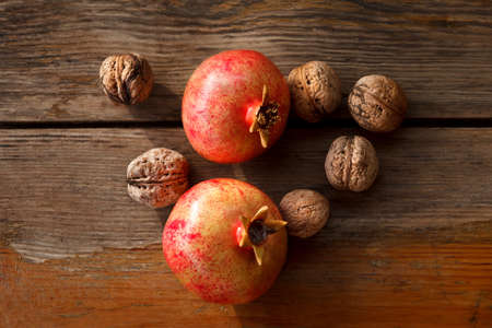 On wooden tanle are two pomegranate and walnuts. The picture is removed from the top. Nuts ripe. Autumn harvest. Pomegranates are large and ripe. Peel pinkish berries with red spots. Aged wooden surface with cracks. The composition is removed in the streeの写真素材
