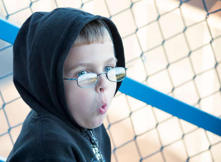 The expression on this little boy's face as he watches his brother playing American Football.  Wearing a black hoody for warmth which frames his face his eyes peeping over his glasses.の写真素材