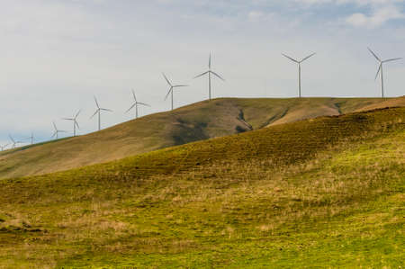 Windturbines stand tall and stark against the high desert landscape of rolling hills in the Columbia River Gorgeの写真素材