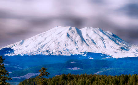 Southside view of Mt. St. Helens.  Layers of clouds in the sky over the snow covered volcano, one of many in the Cascade Mountain Range.の写真素材