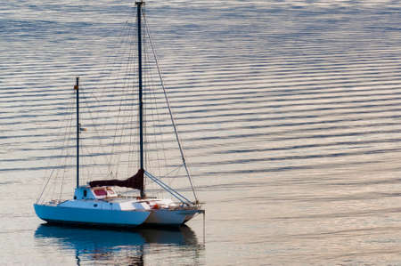 An anchored boat gently rocks on ripples reflecting early dawns rays near the shores of Port Angles, Washington.の写真素材