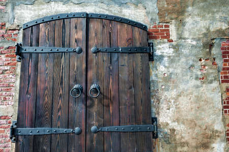 Close up of a heavy wooden plant double door, with iron hinges and handles,closing off the entrance into an old brick building.の写真素材