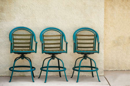 Three outdoor chairs lined up against a stucco wall of an outside wall of a building.の写真素材