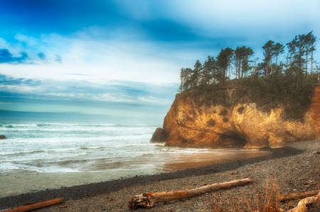 Stormy weather threatens the abandoned beach at Hug Point, Oregon.  The majectic landscape of sculptured shoreline topped with wind shaped trees and washed ashore logs is Oregon's legenary senic coastline.の写真素材