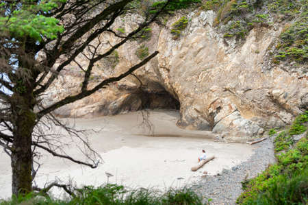 Arch Cape, Oregon - May 15, 2014:  Lady sits on long at Hug Point Beach near Cannon Beach, Oregonのeditorial素材
