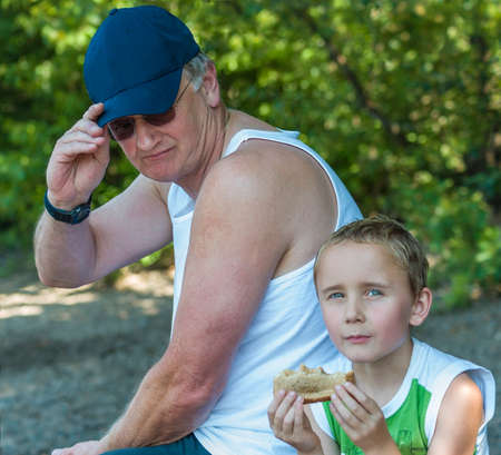 Grandpa and grandson taking a break while grandson eats a sandwhich.の写真素材