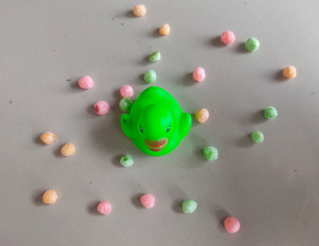 Green rubber duck and multi-colored candies on a gray backgroundの写真素材