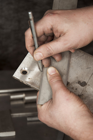 Man`s hands with metal stylus pointing out on a piece of metalの写真素材