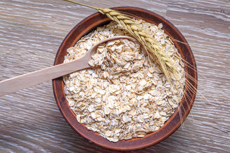 Dry oatmeal in a bowl. An ear of bread lies on the edge of the bowl. Diet porridge is made from...