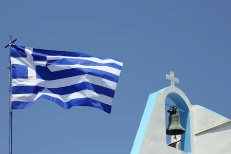bell and cross of a small church and a greek flagの写真素材