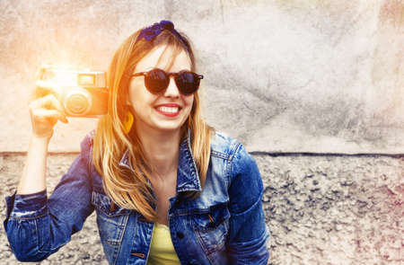 Smiling girl with vintage camera taking photo with flash on wall background. Copy spaceの写真素材