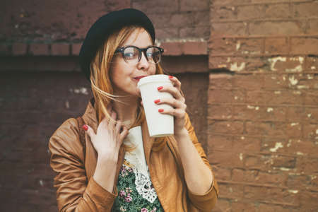 stylish woman drinking coffee on brick wall backgroundの写真素材