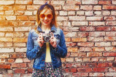 Smiling girl with vintage camera taking photo with flash on brick wall backgroundの写真素材