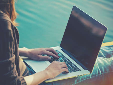girls hands holding laptop in sunlight on natural summer water backgroundの写真素材