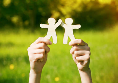 Hands holding wooden little men on natural background. Symbol of friendship, love, teamwork or ecology concept