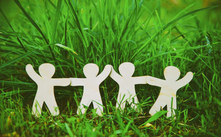 Wooden little men holding hands in summer grass. Symbol of friendship, family, teamwork or ecology concept