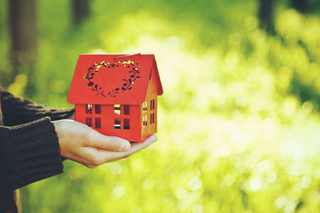hands holding red model of house as symbol on natural garden backgroundの写真素材