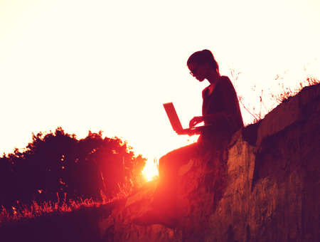 silhouette of a girl with laptop on sunset or sunrise backgroundの写真素材