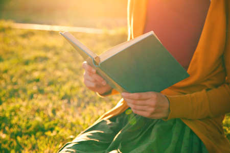 hands holding book and reading in summer sunset lightの写真素材