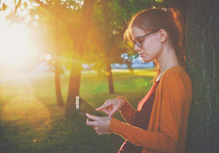 girl holding digital tablet pc at park in summer sunset lightの写真素材